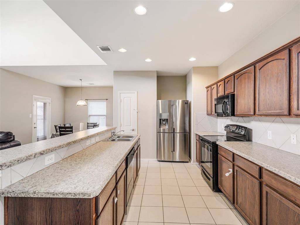 9720 Tipperary Drive, McKinney, TX 75072 Kitchen featuring wood cabinetry, stone-finish countertops, stainless steel appliances, a double-basin sink, and tile flooring