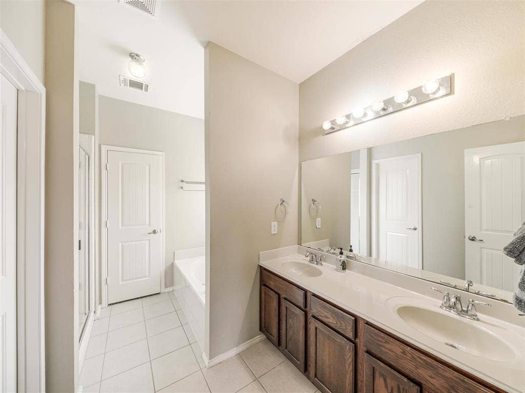9720 Tipperary Drive, McKinney, TX 75072 Dual-sink vanity with dark wood cabinetry, solid-surface countertop, full-width mirror, and integrated lighting