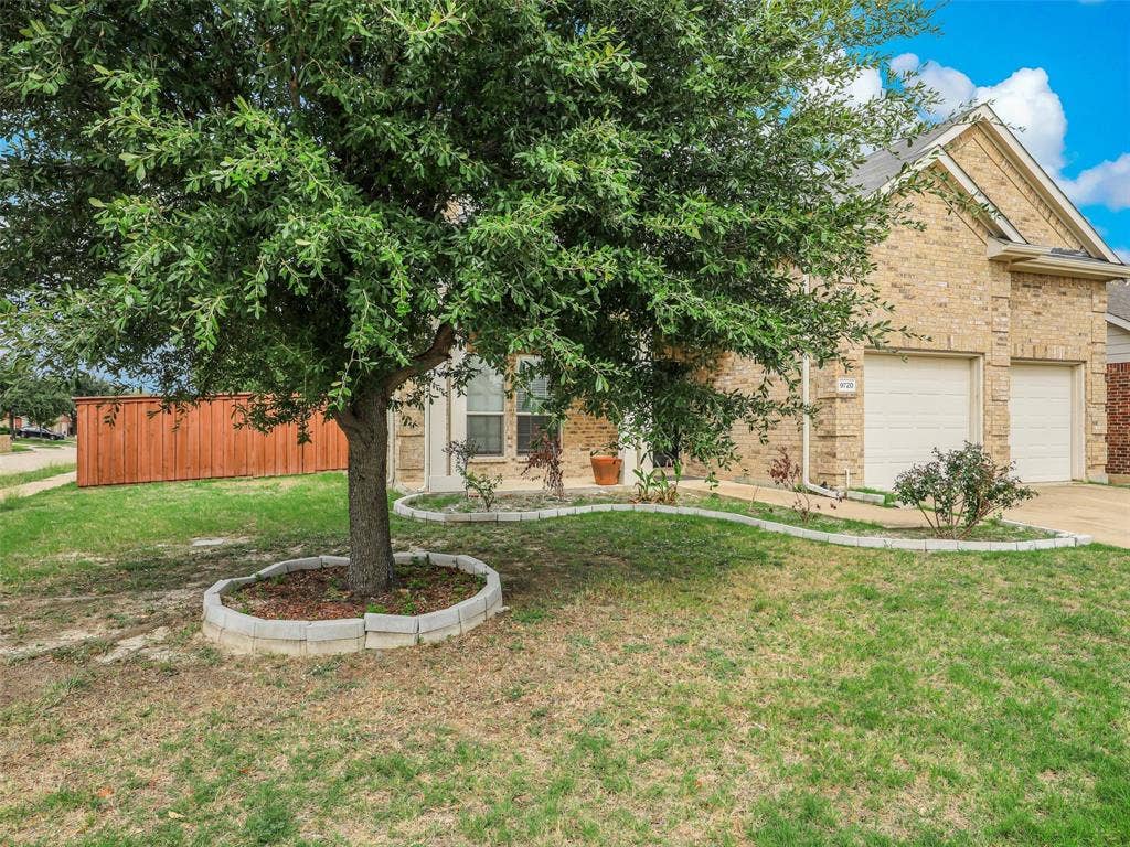 9720 Tipperary Drive, McKinney, TX 75072 Brick exterior featuring a multi-car garage, concrete driveway, and curved stone-bordered garden beds