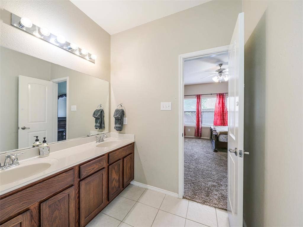 9720 Tipperary Drive, McKinney, TX 75072 Double vanity featuring wood cabinetry, integrated sinks, solid surface countertops, a full-width mirror, and multi-bulb wall lighting