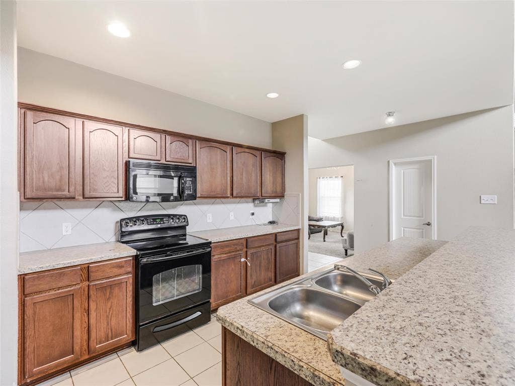 9720 Tipperary Drive, McKinney, TX 75072 Kitchen featuring wood cabinetry, solid surface countertops, a dual-basin stainless steel sink, tile backsplash, and built-in black appliances