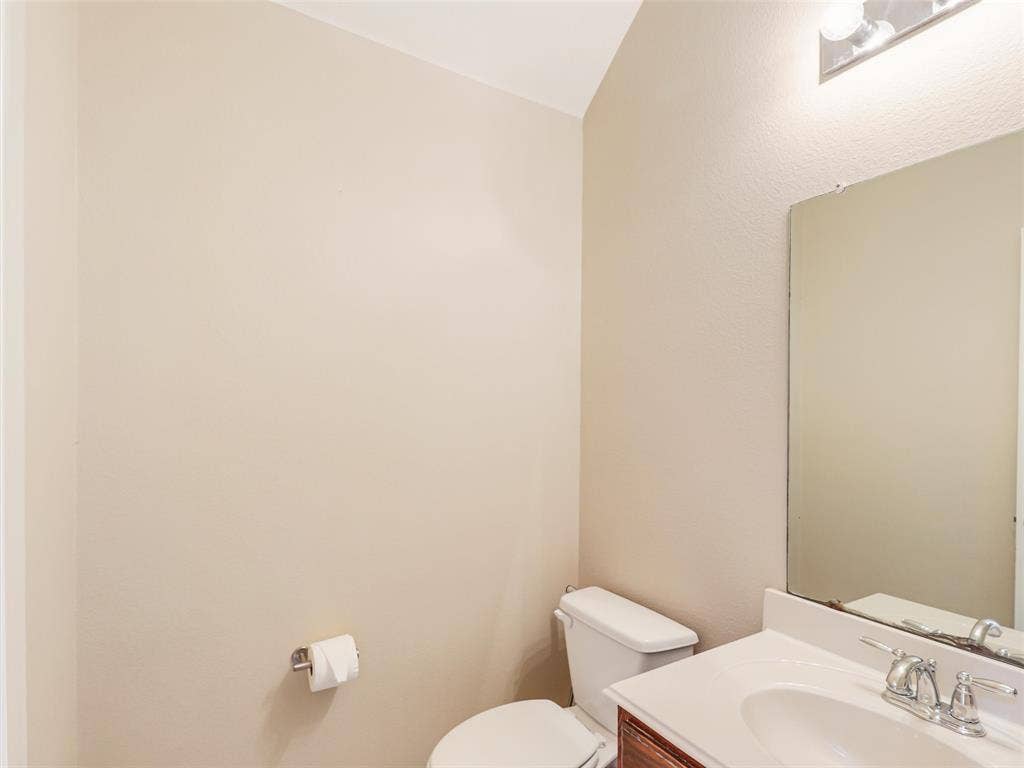9720 Tipperary Drive, McKinney, TX 75072 Wall-mounted vanity featuring a solid surface countertop, integrated oval basin, metallic faucet, large rectangular mirror, and overhead light fixture