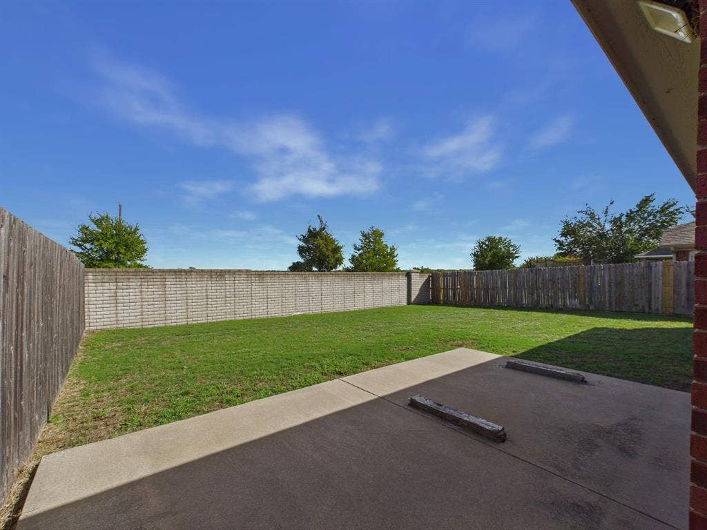Rear concrete patio featuring wheel stops, grass lawn, and perimeter wood and masonry fencing