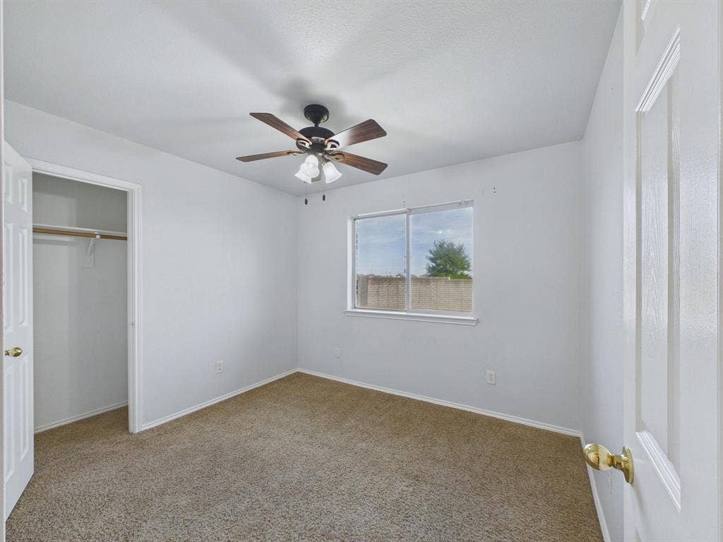 Neutral-toned carpeting, ceiling fan with integrated lighting, slider window, and built-in closet