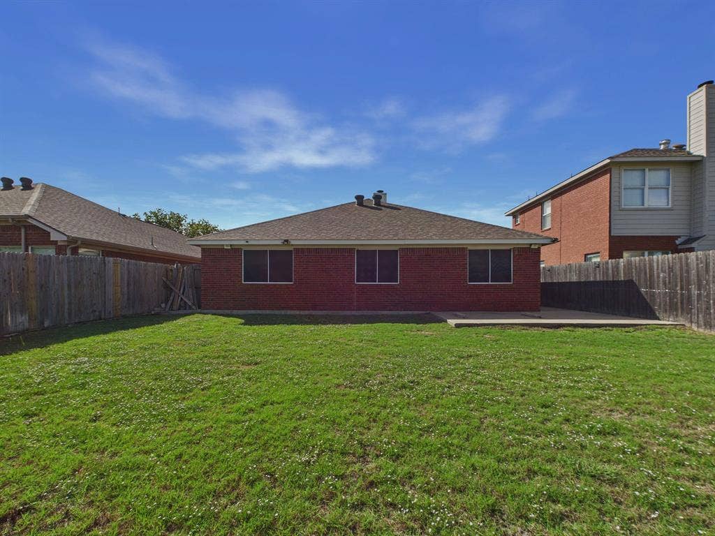 Rear exterior featuring a brick facade, concrete patio, and fenced backyard with grass lawn