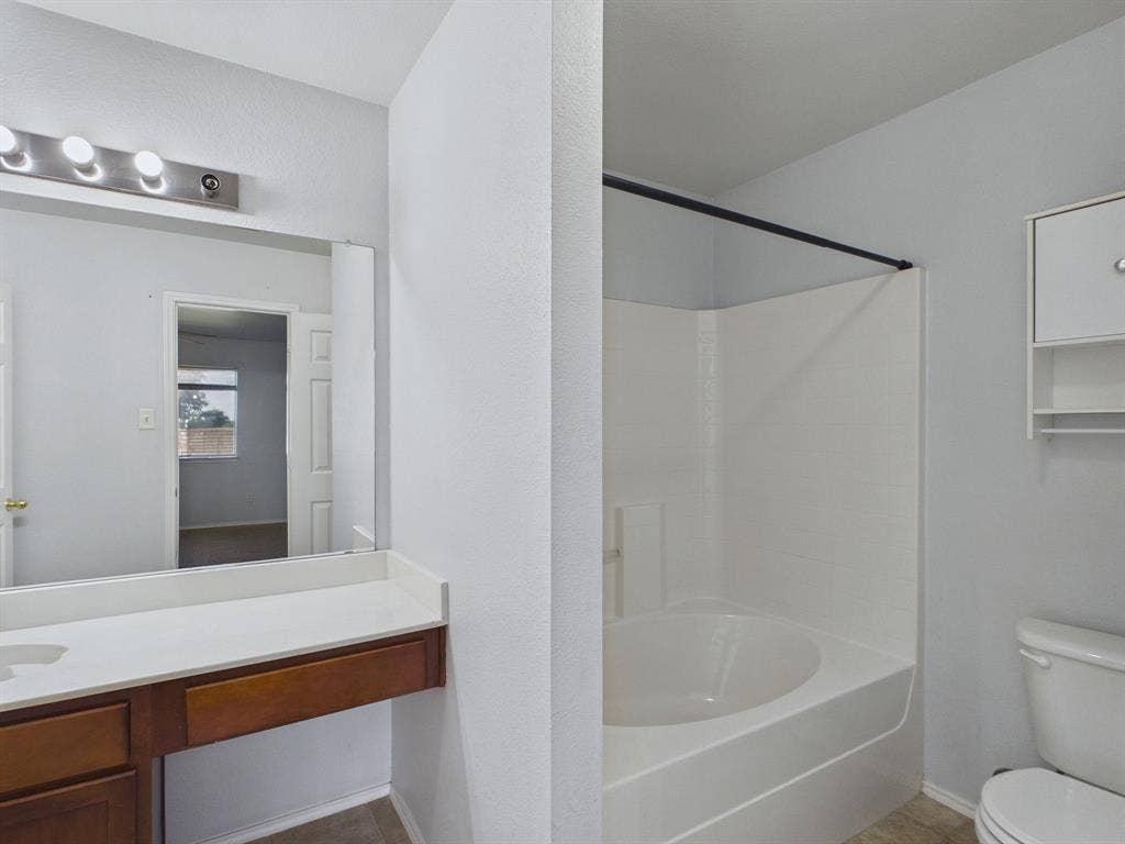 Bathroom featuring a white vanity with a rectangular sink, wall-mounted light fixture, full-width mirror, and a built-in tub-shower combination with a matte black shower rod