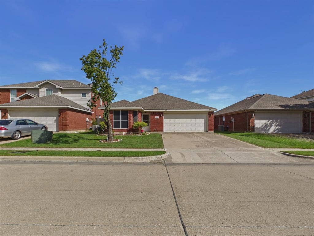 Single-story brick exterior featuring a shingle roof, multi-panel garage door, concrete driveway, and front lawn landscaping