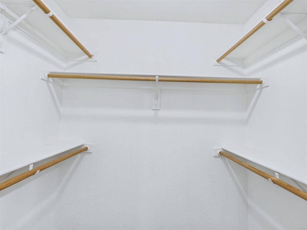 Walk-in storage space featuring multi-level white shelving and integrated natural wood-finish hanging rods