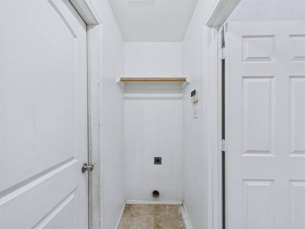Utility alcove featuring tile flooring, a wall-mounted shelf with a rod, and dedicated appliance hookups