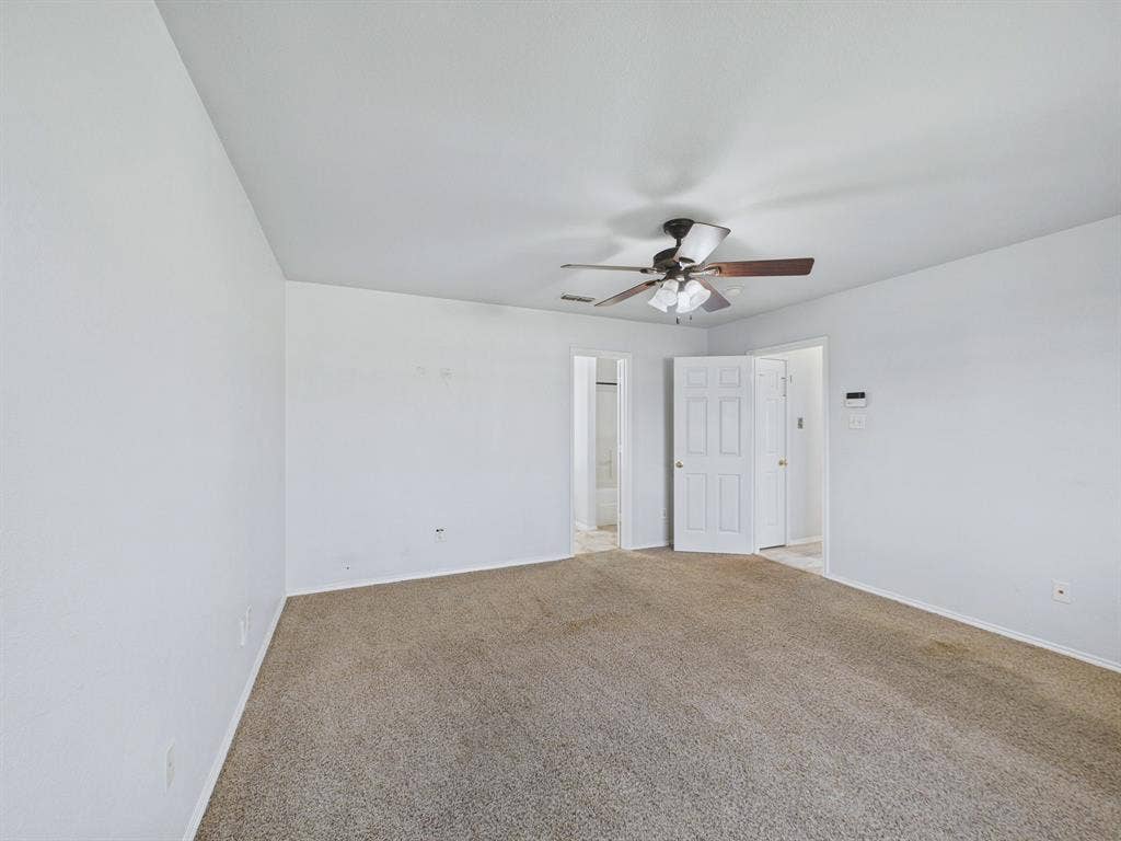 Spacious interior room featuring neutral carpeting, a ceiling fan with integrated light fixture, and white six-panel interior doors
