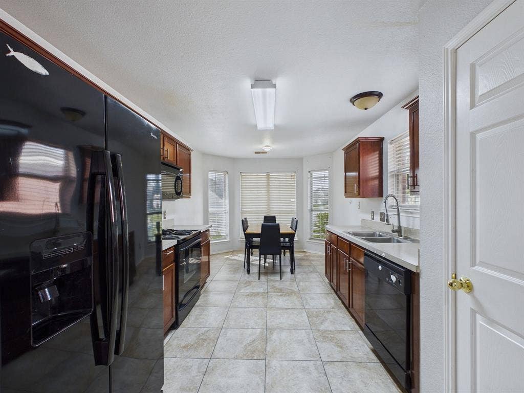 Kitchen featuring wood cabinetry, solid surface countertops, tile flooring, built-in black appliances, and a bay window configuration
