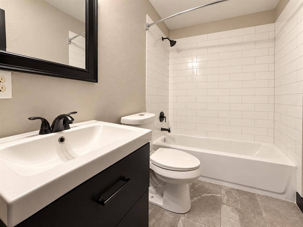 1817 N Alexander Street, Sherman, TX 75092 Updated bathroom featuring a modern vanity, subway tile tub surround, and coordinating dark fixtures.