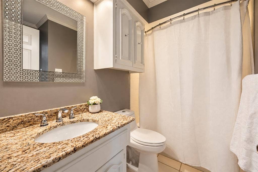 5833 Gallant Fox Lane, Plano, TX 75093 Bathroom featuring a stone-surface countertop, white cabinetry with upper storage, undermount sink with dual-handle faucet, and patterned decorative mirror