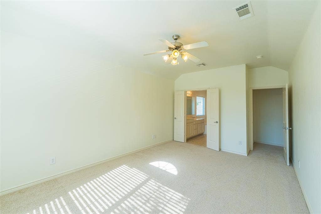 Interior space featuring neutral wall-to-wall carpeting, vaulted ceiling, multi-blade ceiling fan with integrated lighting, and dual-panel interior doors