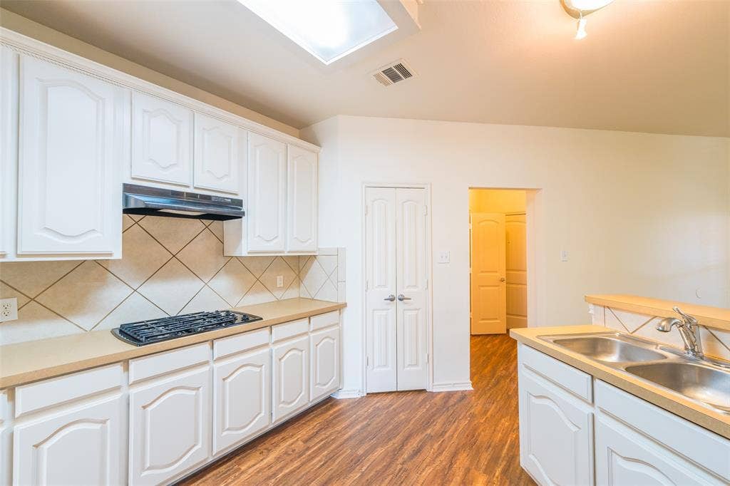 Kitchen featuring white cabinetry, a neutral solid-surface countertop, an inset gas cooktop with a range hood, a dual-basin stainless steel sink, and wood-finish flooring