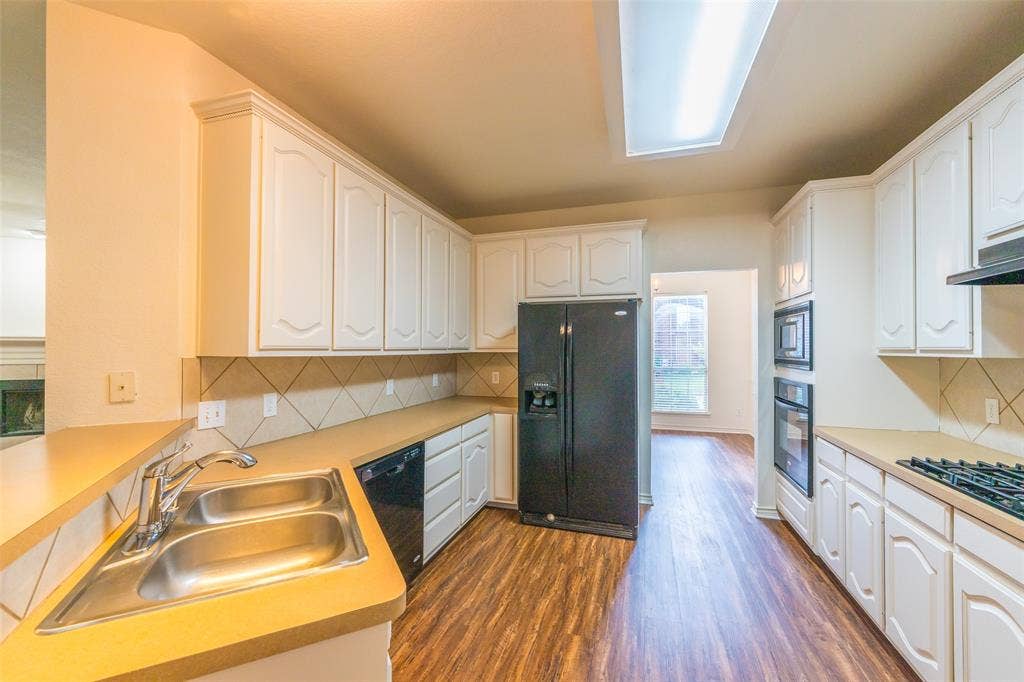 Kitchen featuring white cabinetry, wood-finish flooring, a recessed skylight, solid-surface countertops, and built-in wall appliances