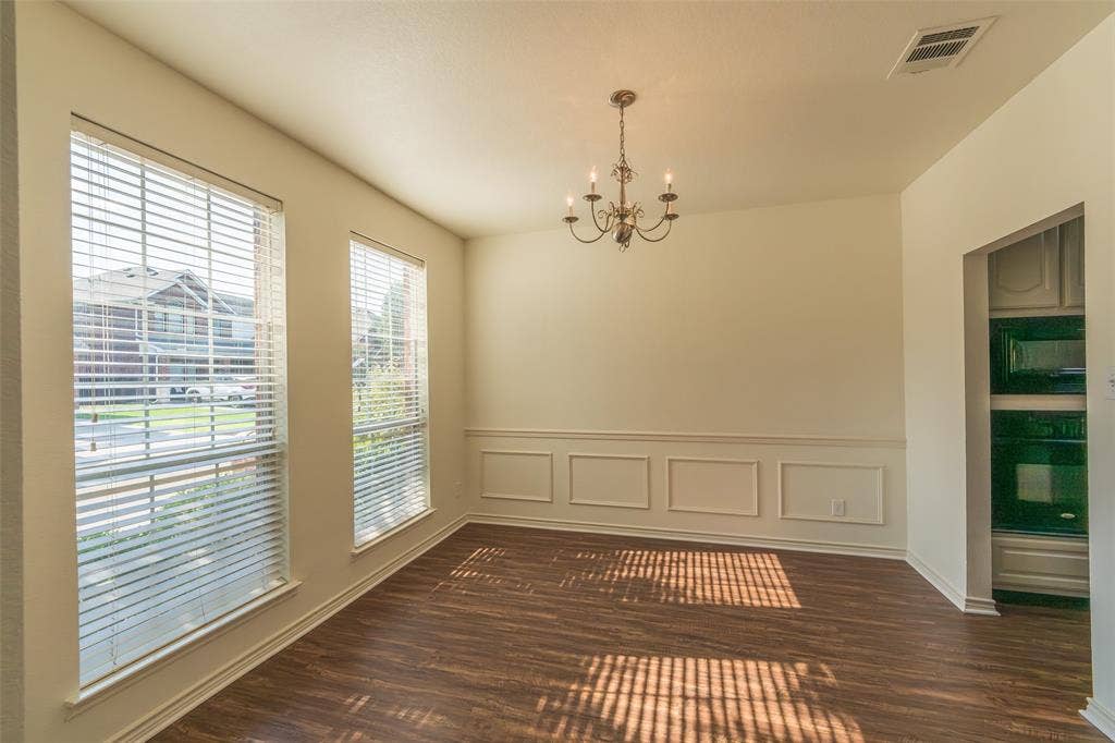Room featuring wood-finish flooring, wainscoting, large windows with blinds, a multi-arm chandelier, and built-in wall oven cabinetry