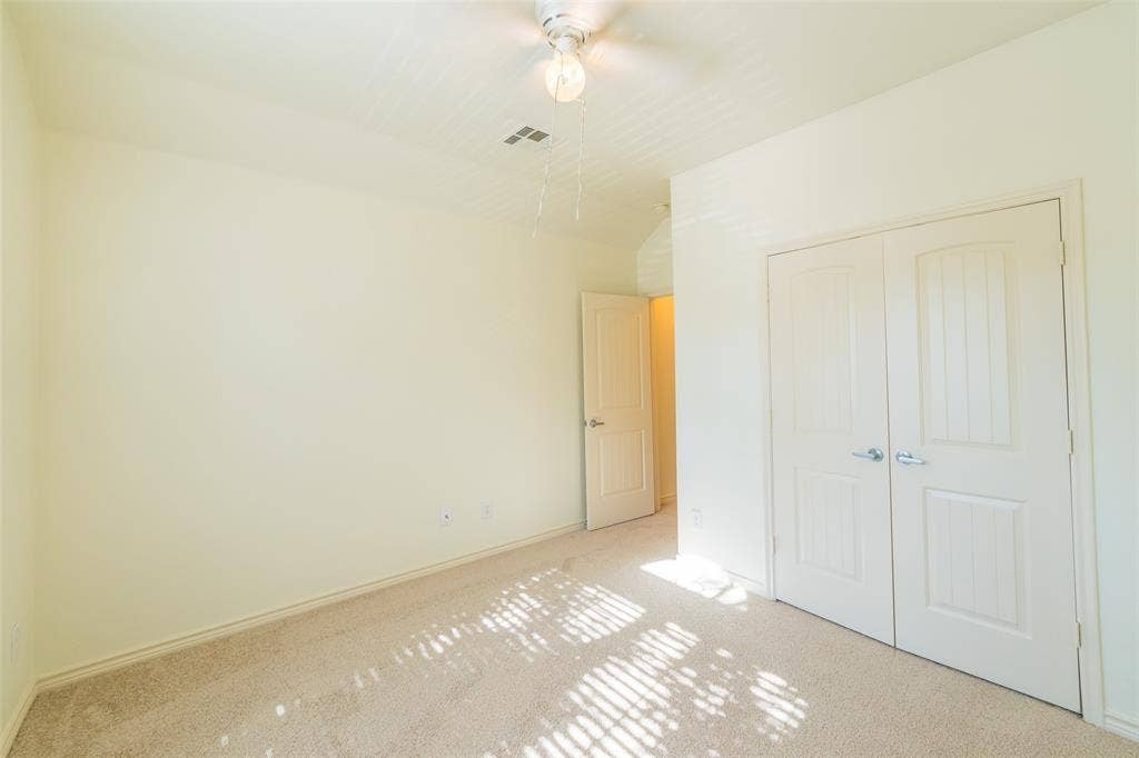 Neutral-toned wall-to-wall carpeting, dual-panel closet doors, single-panel interior door, and a ceiling fan with integrated lighting