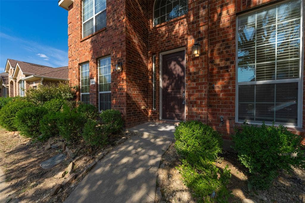 Red brick exterior featuring an arched window, multi-pane glass windows, concrete walkway, and wall-mounted exterior lighting