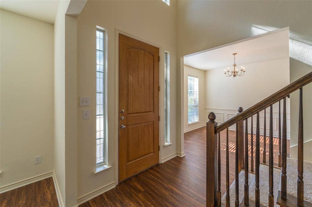 Foyer featuring wood-finish flooring, a solid wood door with decorative glass sidelights, and a staircase with a stained wood handrail and balusters