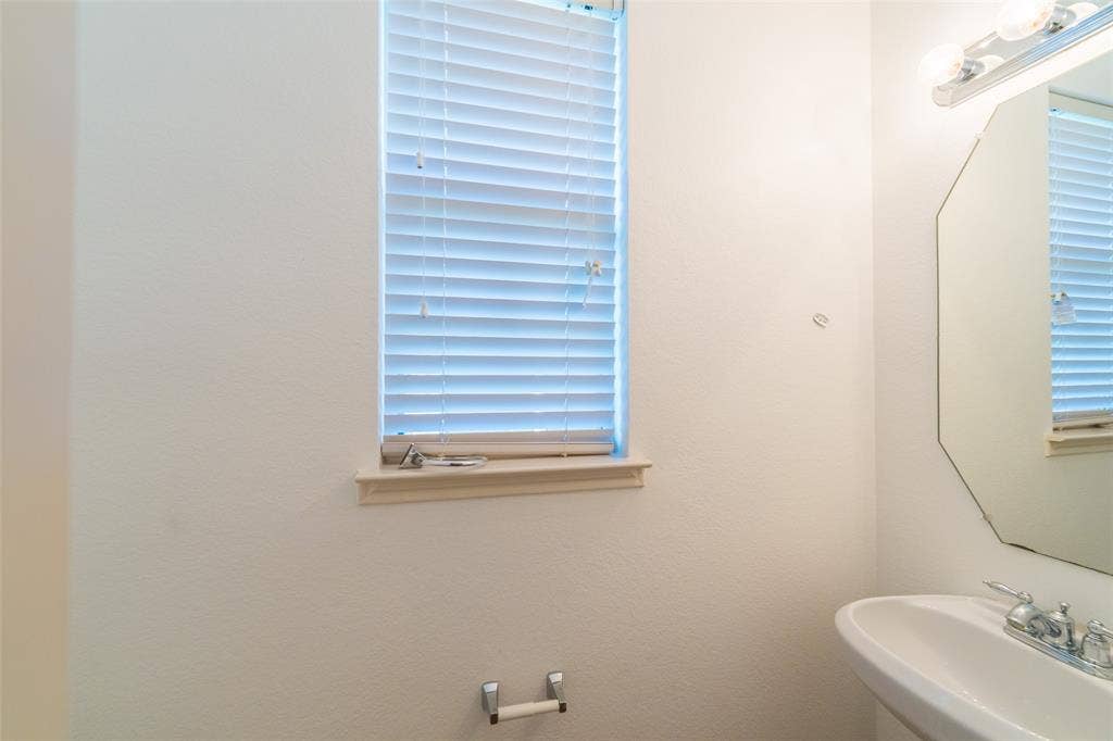 Octagonal wall-mounted mirror, pedestal sink with chrome faucet, window with integrated blinds, and chrome hardware fixtures