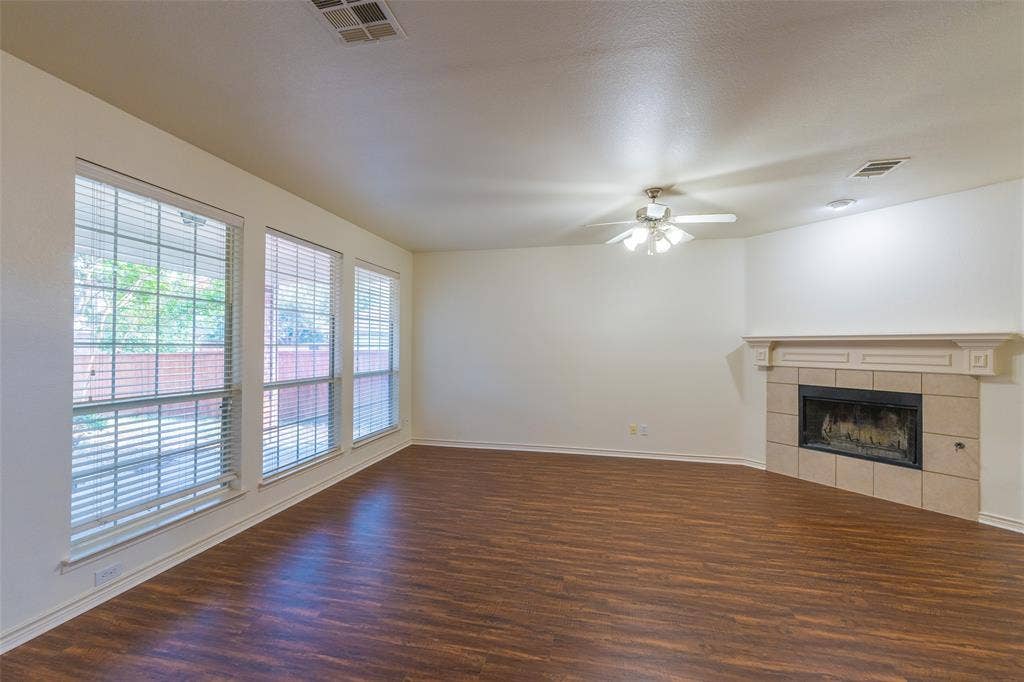 Living area featuring wood-finish flooring, a corner fireplace with a decorative mantel and stone-finish surround, triple pane windows, and a ceiling-mounted light fixture