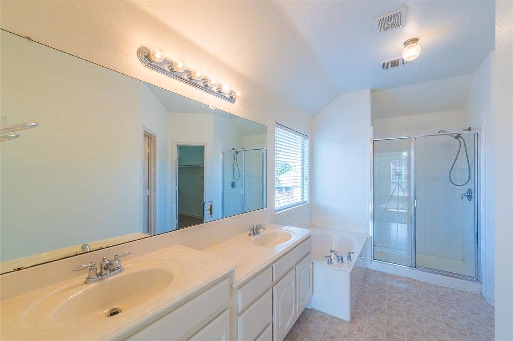Double vanity with integrated sinks, expansive wall-to-wall mirror, built-in soaking tub, and a separate glass-enclosed shower