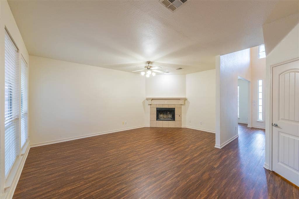 Living area featuring wood-finish flooring, a corner fireplace with a decorative mantel, ceiling fan with light fixture, and vertical windows with blinds