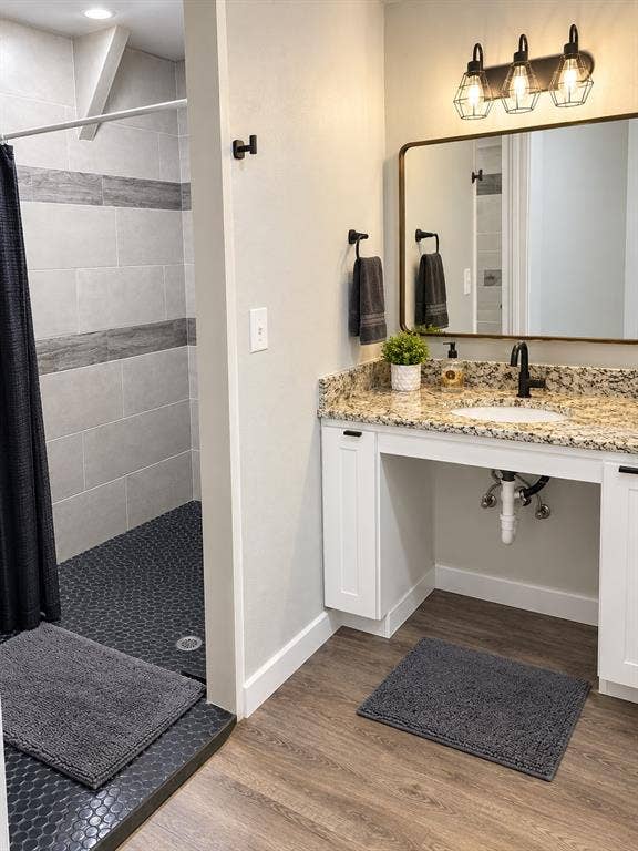 1579 Eastside Lake Road, Graham, TX 76450 Bathroom featuring a granite countertop, white shaker-style cabinetry, a brass-framed rectangular mirror, three-light industrial vanity fixture, and a tiled shower stall with hex-patterned flooring