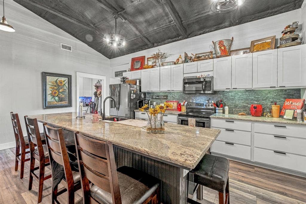 1579 Eastside Lake Road, Graham, TX 76450 Kitchen featuring white Shaker-style cabinetry, a large granite-topped island with an integrated sink, vaulted ceilings, and wood-finish vinyl flooring