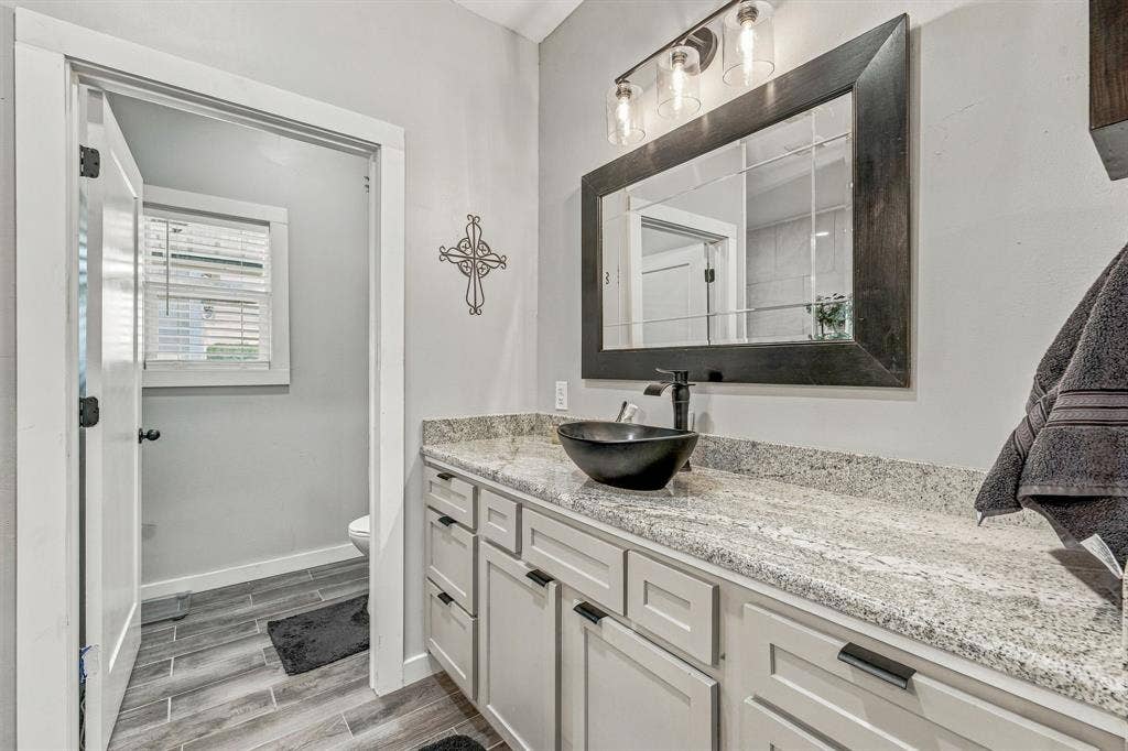 1579 Eastside Lake Road, Graham, TX 76450 Light-toned vanity cabinetry topped with granite-finish countertop, dark vessel sink, matte black faucet, and wood-finish tile flooring