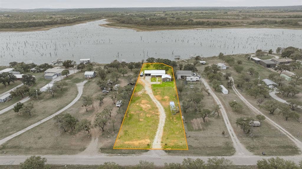1579 Eastside Lake Road, Graham, TX 76450 Aerial perspective of a waterfront property featuring a long private driveway, open acreage, and mature trees