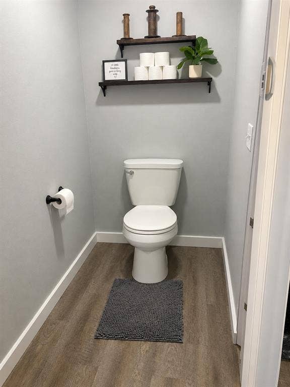 1579 Eastside Lake Road, Graham, TX 76450 Water closet featuring wood-finish flooring, a two-piece toilet, and a matte black toilet paper holder