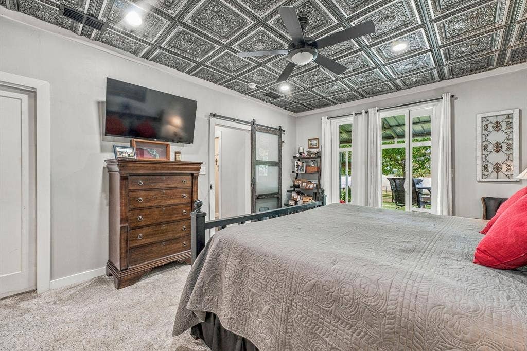 1579 Eastside Lake Road, Graham, TX 76450 Detailed decorative ceiling tile, matte black ceiling fan with integrated lighting, sliding barn door with frosted glass panel, and floor-to-ceiling glass sliding door with exterior access