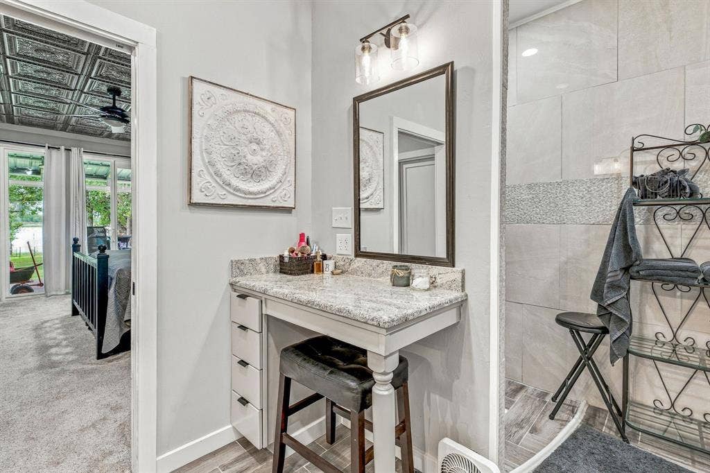 1579 Eastside Lake Road, Graham, TX 76450 Built-in vanity with stone countertop, multi-drawer cabinetry, framed wall mirror, dual-bulb vanity lighting, and tiled walk-in shower