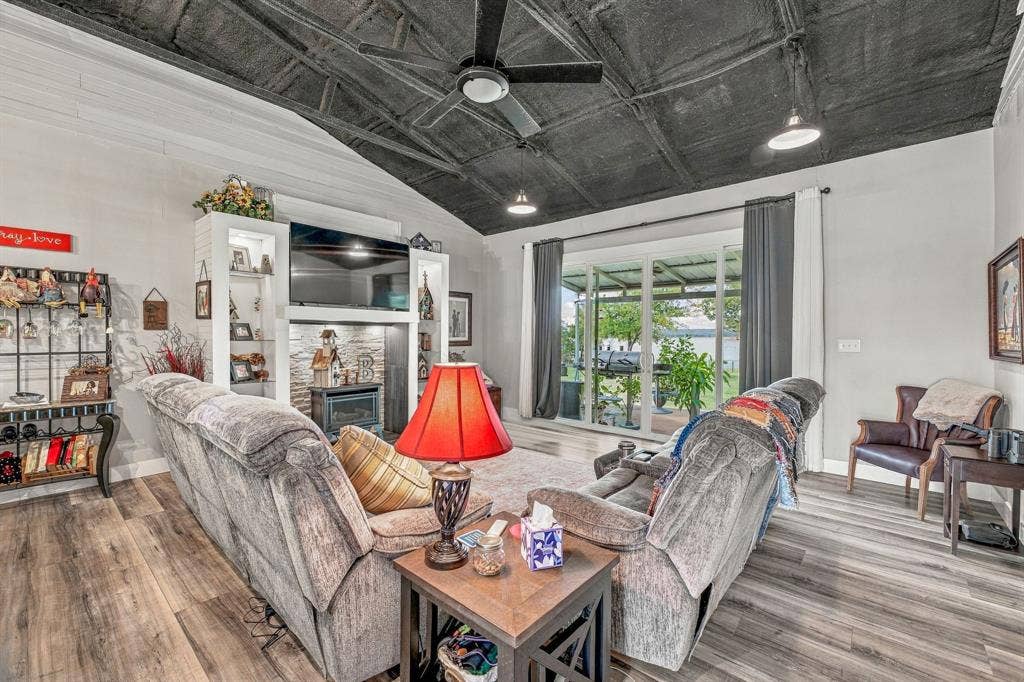 1579 Eastside Lake Road, Graham, TX 76450 Living area featuring an exposed rafter ceiling, wood-finish vinyl flooring, floor-to-ceiling built-in shelving with an integrated propane fireplace, and sliding glass doors opening to covered back porch
