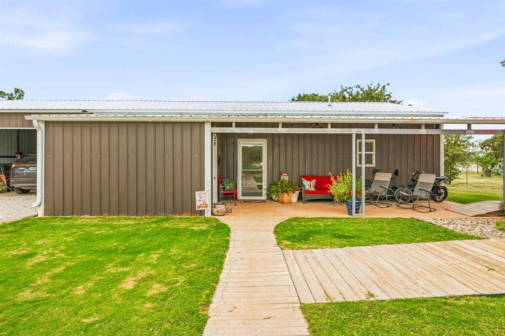 1579 Eastside Lake Road, Graham, TX 76450 Metal-siding exterior featuring a covered front porch, corrugated metal roof, integrated garage, and wood-plank style walkway