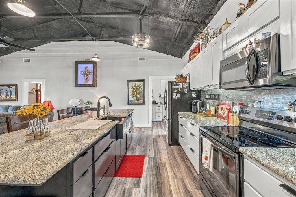 1579 Eastside Lake Road, Graham, TX 76450 Kitchen featuring granite countertops, an expansive center island with an integrated farmhouse sink, wood-finish flooring, white shaker-style cabinetry, and vaulted ceilings with exposed beams