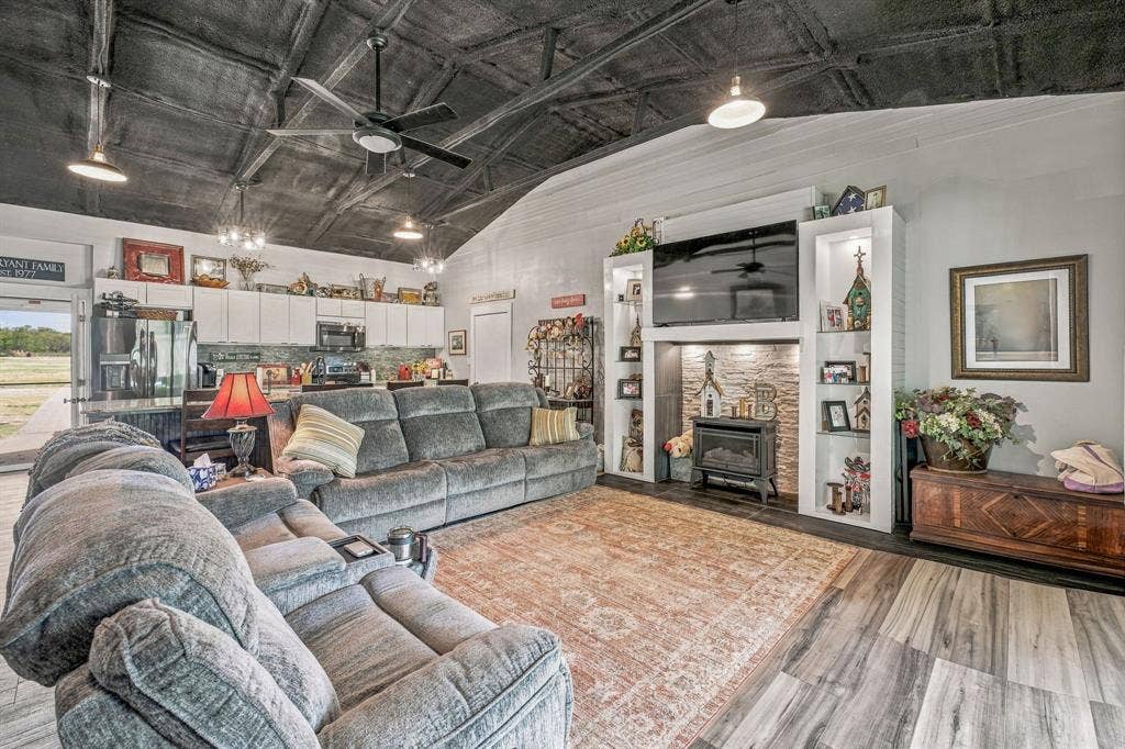 1579 Eastside Lake Road, Graham, TX 76450 Vaulted ceiling with exposed structural elements, wood-finish vinyl flooring, built-in entertainment center with integrated shelving, stone-surround fireplace insert, and contemporary pendant lighting