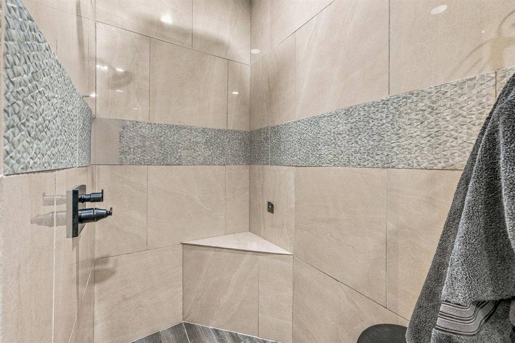 1579 Eastside Lake Road, Graham, TX 76450 Walk-in shower featuring large-format beige tile, decorative horizontal stone-texture accent inlay, built-in corner bench, and matte black wall-mounted shower fixtures