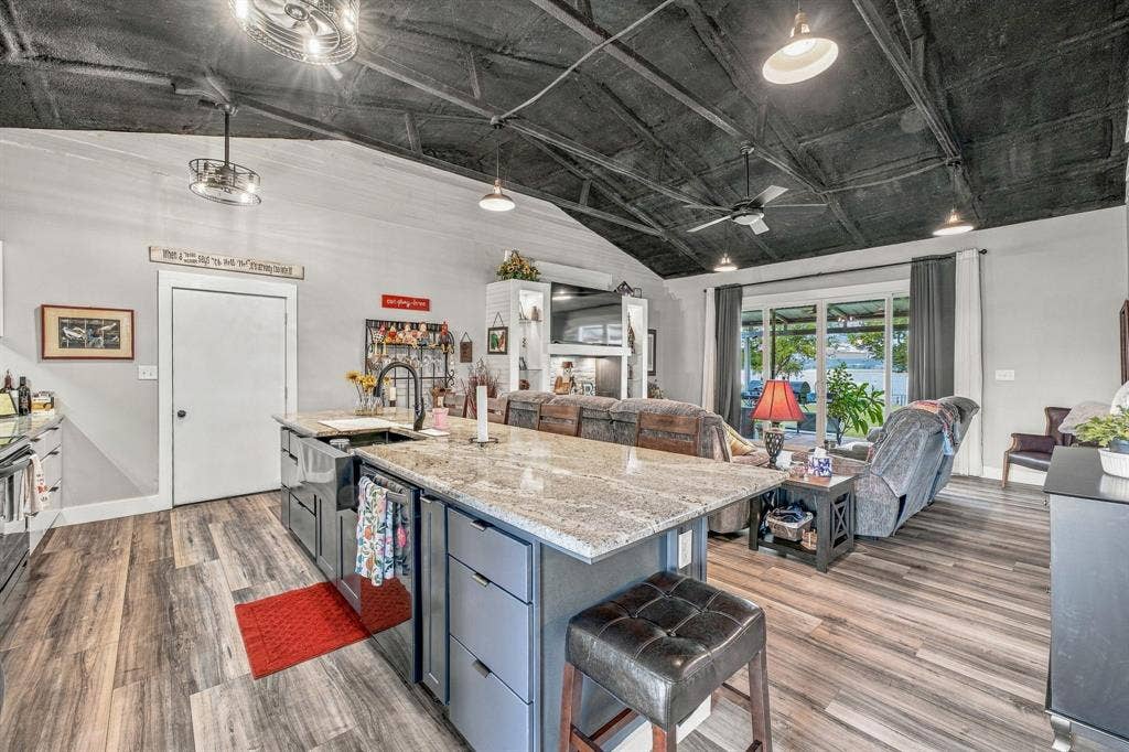 1579 Eastside Lake Road, Graham, TX 76450 Vaulted ceiling with exposed structural beams, kitchen island with granite countertop, apron-front sink, wood-finish vinyl flooring, and integrated pendant and track lighting