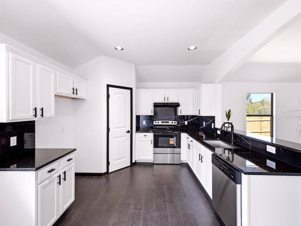 Kitchen featuring white shaker-style cabinetry, dark stone countertops, a full-height stone backsplash, stainless steel appliances, and dark-toned flooring