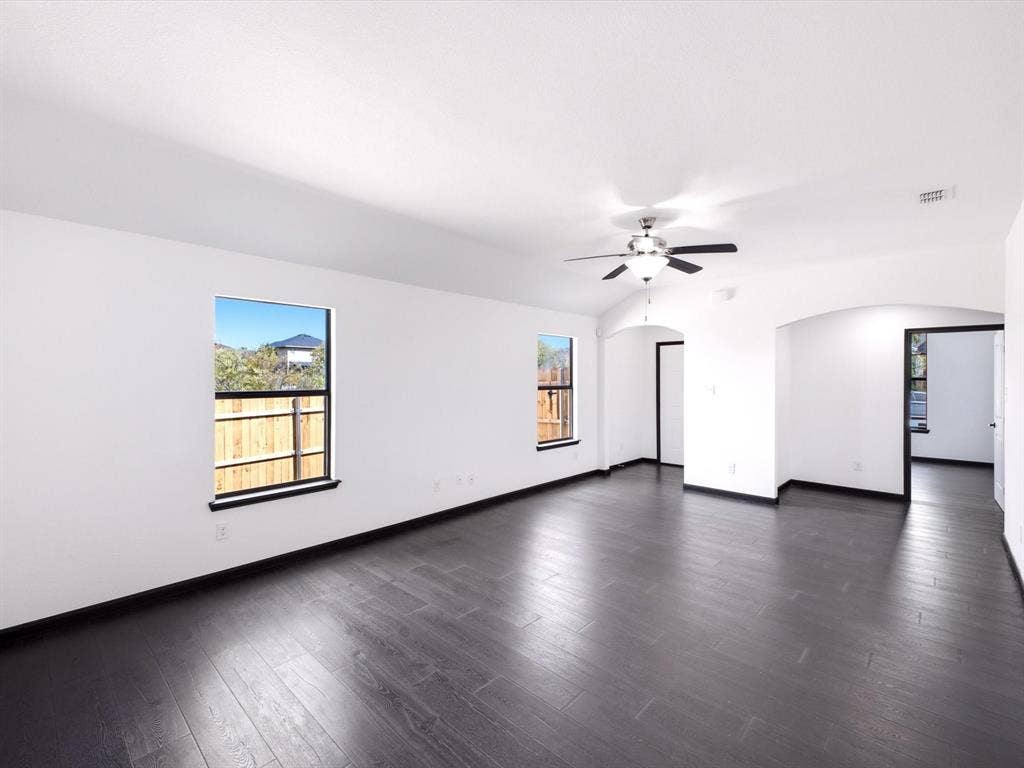 Interior space featuring dark wood-finish flooring, vaulted ceiling with a central light-integrated ceiling fan, two windows, and prominent arched architectural openings