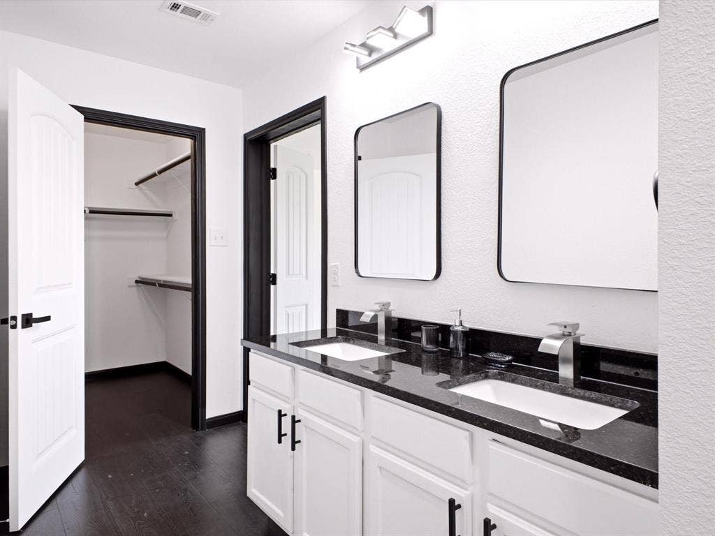 Dual-sink vanity with dark stone countertop, undermount sinks, matte black cabinet hardware, framed mirrors, and dark wood-finish flooring