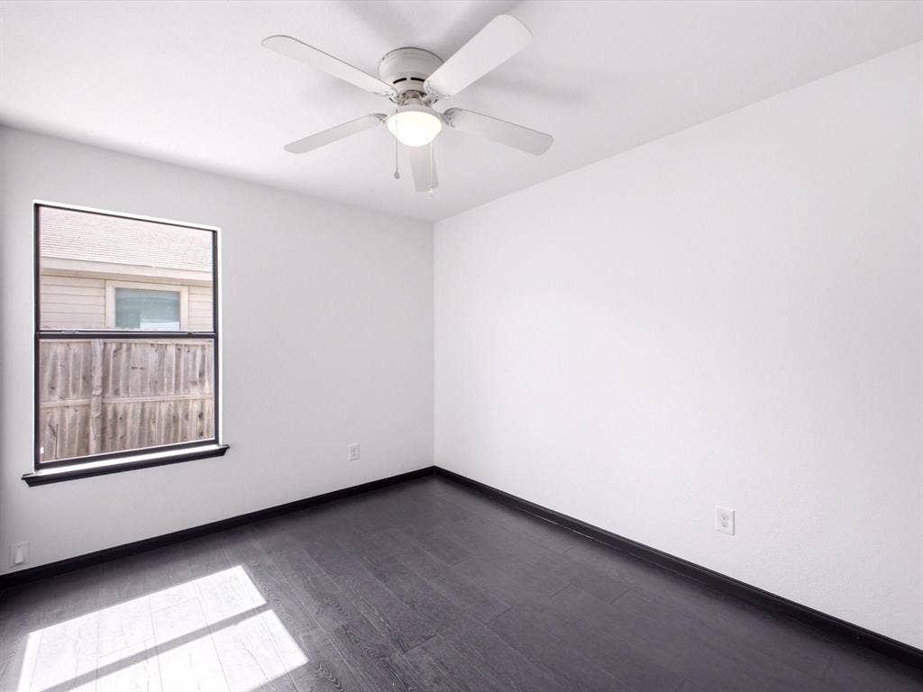 Room featuring dark wood-finish flooring, white walls, a single-hung window, and a ceiling fan with integrated lighting