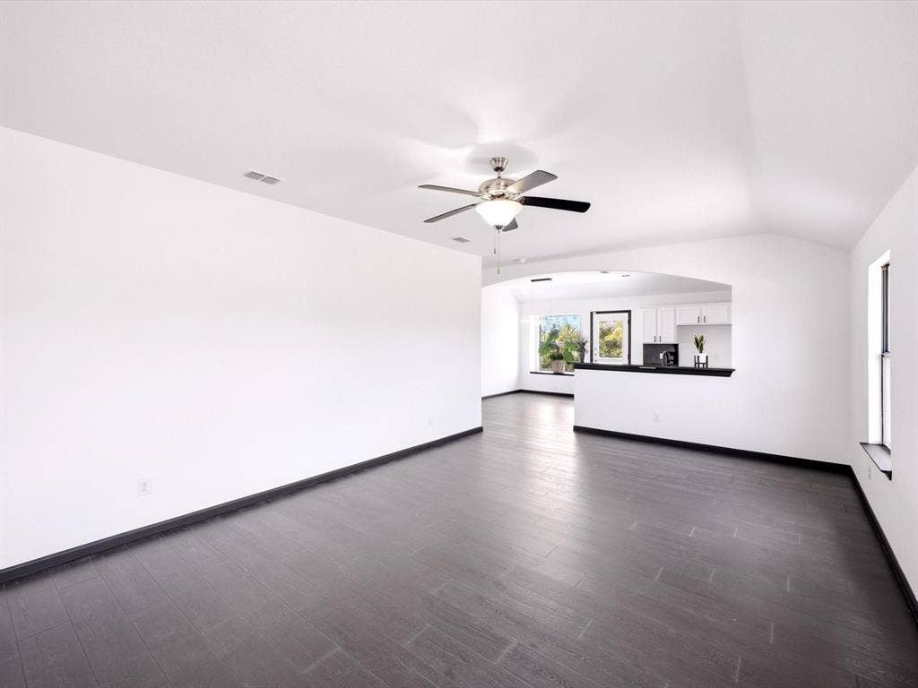Vaulted ceilings, wood-finish flooring, recessed lighting, and a brushed nickel ceiling fan with integrated light fixture, featuring a partition wall with a pass-through opening
