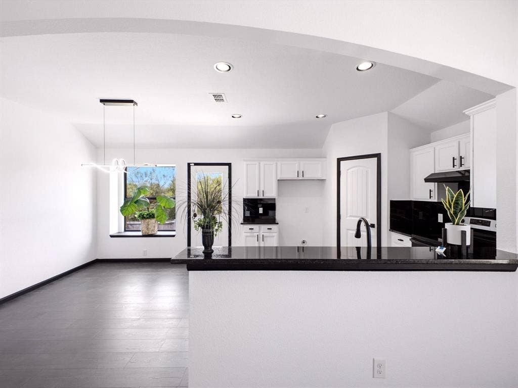 Kitchen featuring white shaker-style cabinetry, high-contrast black countertops, a deep-tone kitchen sink with a matte black faucet, recessed ceiling lighting, and large-format tile flooring