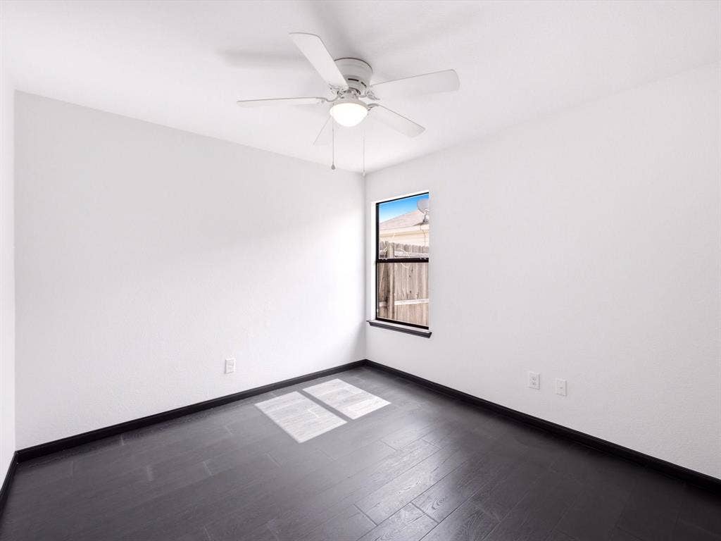 Room featuring dark wood-finish flooring, white walls, a ceiling fan with integrated light fixture, and a single-pane window