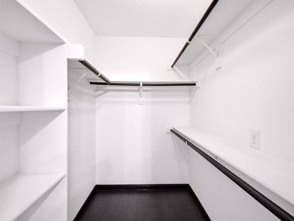 Walk-in closet featuring multi-level hanging rods, integrated wall shelving, and dark-finish flooring