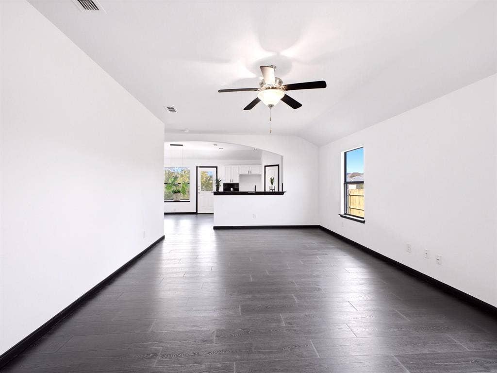 Interior space featuring dark wood-finish flooring, vaulted ceilings, a central ceiling fan with integrated lighting, and a pass-through opening